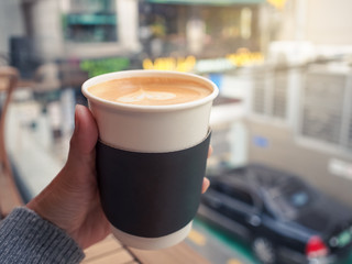 Female hand holding a paper cup of hot coffee, selective focus.