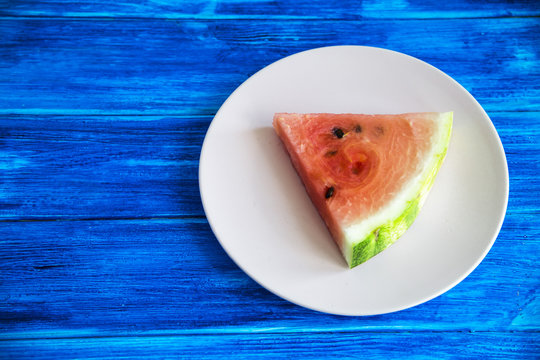 A triangular slice of watermelon on a pink plate on a blue wooden background