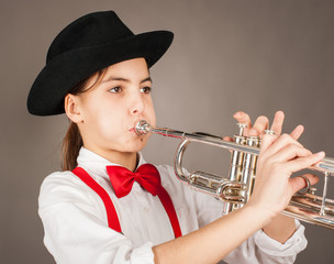 little girl playing trumpet on a gray background