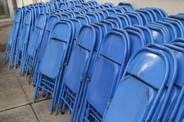 stacks of blue folding chairs against a wall outside a concert area