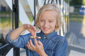 Cheerful cute school aged girl playing with a gold fidget spinner. A popular trendy toy.