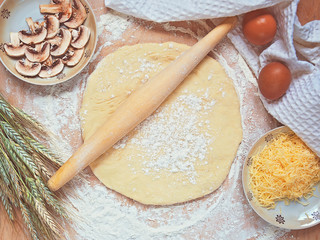 Pizza cooking, top view. Rolling pin on the dough sprinkled by wheat flour.