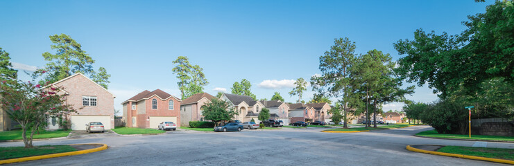 Suburban residential area, row of modern townhomes in Humble, Texas, US. Red brick houses surrounded with tall pine trees, cloud blue sky. Panorama view street intersection and multi-story townhouses. - obrazy, fototapety, plakaty