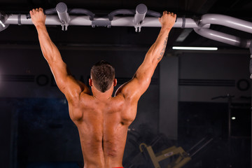 Fototapeta na wymiar Rear view of muscular man doing pull ups at the gym