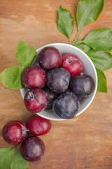 Ripe red and blue plums in a bowl on a wooden table
