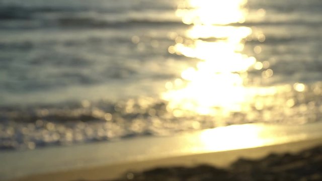 Defocused romance background, sunset waves splashing on a beach as a couple walks by