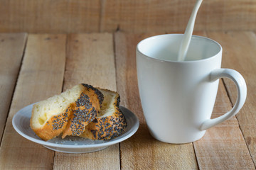 Crackers with poppy seeds on a plate. Milk is poured into a white mug.Wooden table.