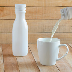 Milk and yogurt are poured into a white mug from the bottle.Tableware stands on a wooden table.