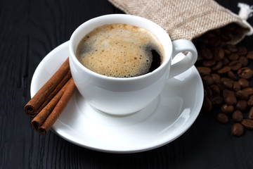 Fresh coffee with foam in a white cup with cinnamon and a bag of grains