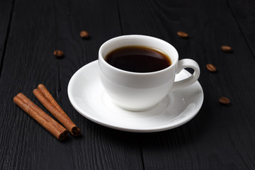 Coffee in a white cup with cinnamon sticks on a black background