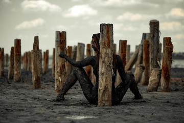 Young woman smeared with therapeutic mud and sits near wooden column.