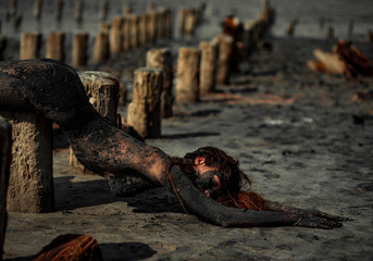 Young woman smeared with therapeutic mud and lies on wooden column.