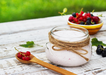 Yogurt in a jar and a saucer with berries on a table in the fresh air