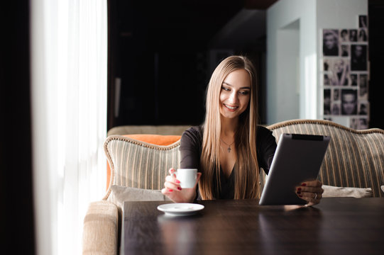 Happy young woman drinking coffee / tea and using tablet computer in a coffee shop