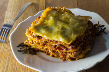 Traditional lasagna made with minced beef bolognese sauce and bechamel sauce topped with mozarella close up romantic rustic dinner