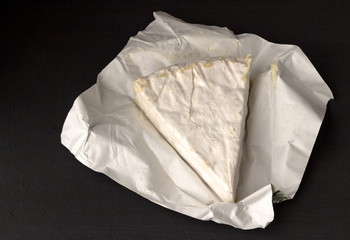 Brie type of cheese. Camembert cheese. Fresh Brie cheese wedge uncut on black background with text...