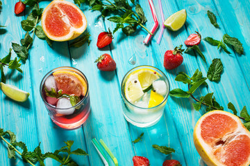 Glass of alcohol cold coctail decorated with ice, fruit and mint staying on wood table. Fresh juice on background with lemon, strawberry, lime