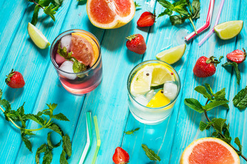 Glass of alcohol cold coctail decorated with ice, fruit and mint staying on wood table. Fresh juice on background with lemon, strawberry, lime