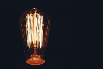 Close-up of glowing retro light bulb on a black background. Copy space.