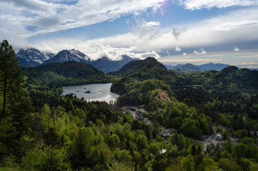Panorama of the  Alpsee lake and its forest, under a partially cloudy sky, with the romantic medieval-style castle of Hohenschwangau, in Bavaria, Germany.