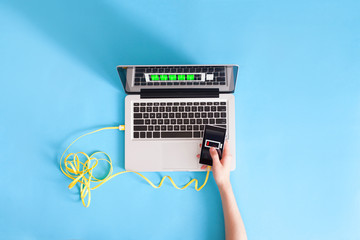 Women hands holding phone with low charged battery screen charging from laptop