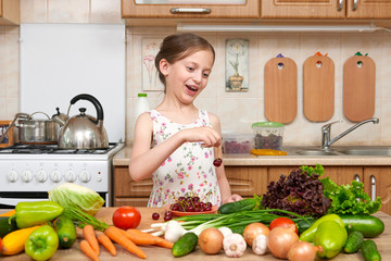 child girl posing with cherry, fruits and vegetables in home kitchen interior, healthy food concept