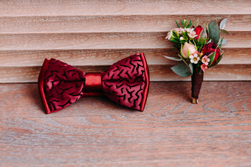 Stylish red bow and boutonniere on wooden background, groom getting ready in morning before the...