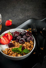Healthy breakfast. Summer berries and fruits. Homemade Greek yogurt with granola, blackberries, strawberries and mint. On a black stone table, with the ingredients.