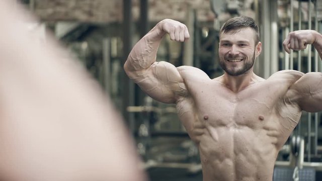 A bodybuilder with a tattoo makes a pose with a double bicep in front. The athlete with a beard performs a mandatory classic element of posing in bodybuilding. The arms and legs are tense, the press