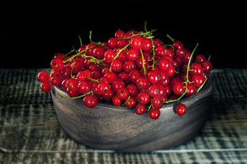 Wooden utensils with ripe red currant berries on a dark background.