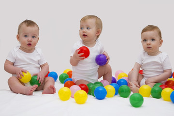 Fototapeta na wymiar Funny baby triplets smiliing and playing with colorful balls. Studio shot