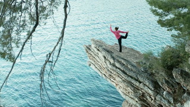 Yoga coach Stunning views of the cliff and a woman who is doing exercises at sea. On a high ledge stone