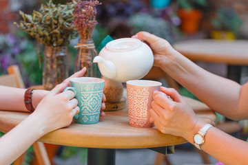 Two girl-friends talk and drink tea in cafe, outdoors