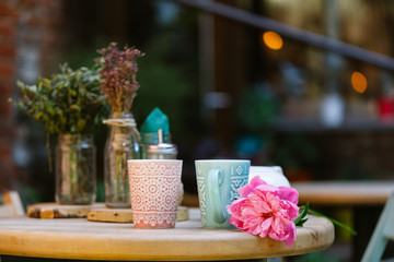 cups of tea and peony on wooden table in street cafe