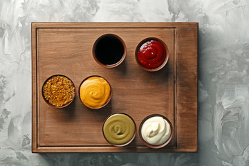 Wooden board with different sauces on grunge background