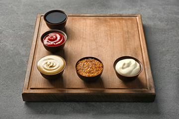 Wooden plate with different sauces on gray background