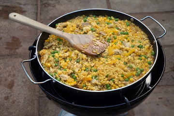 Paella with chicken, peas, sweetcorn and pepper cooking on an outdoor camping cooker