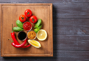 Wooden plate with different sauces and vegetables on table