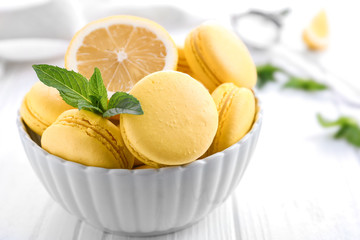 Bowl with tasty lemon macarons on white wooden table, closeup