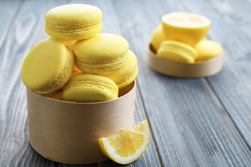 Box with tasty lemon macarons on wooden table, closeup