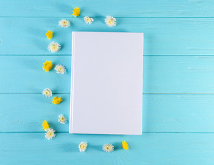 Fototapeta premium Book with blank white cover and beautiful flowers on color wooden background