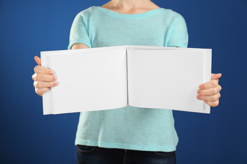 Woman holding open book with blank pages on color background