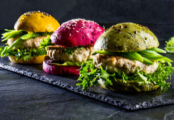 Colored green, yellow and purple burgers on slate board, slate background