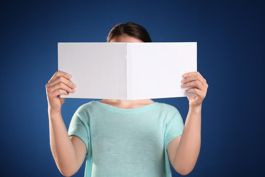 Woman holding open book with blank cover on color background