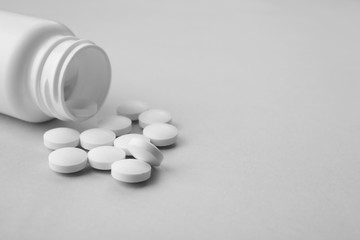 Plastic container and pills on light background