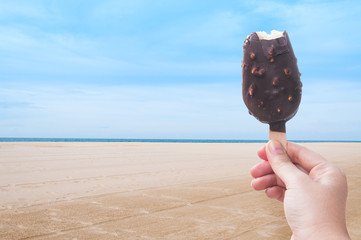 Woman hand holding chocolate ice cream in the summer at the beach, during the holidays