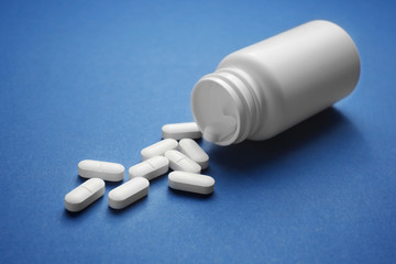 Plastic container and pills on blue background