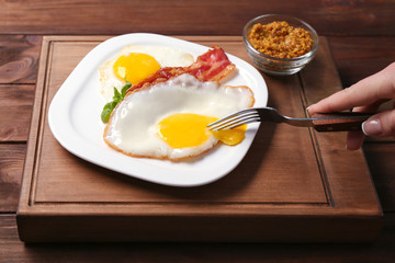 Woman eating over easy eggs with bacon at table