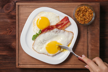 Woman eating over easy eggs with bacon at table
