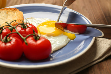 Knife and fork with delicious over easy egg on plate, closeup